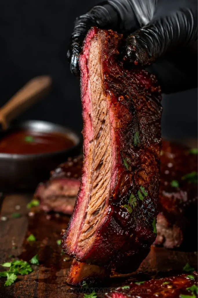Single beef baby back rib showing pink smoke ring and dark caramelized bark after slow cooking