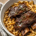 raised beef short ribs served over egg noodles with rich brown sauce in a white bowl