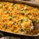 Chicken broccoli rice casserole in a golden baking dish with a buttery Ritz cracker crust and melted cheddar cheese, served with a wooden spoon